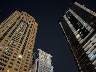 Modern high-rise buildings against dark night sky. Urban architecture and city lifestyle concept, view from below.