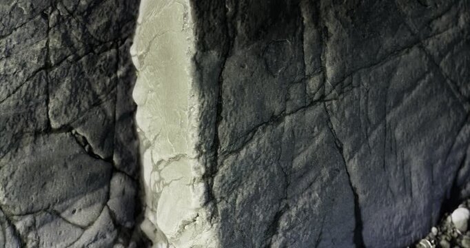 In a quiet, secluded area, sunlight gently illuminates a rugged rock surface, revealing detailed textures and shadows. This serene setting highlights natures artistry over time.