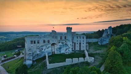 Aerial photograph showing the medieval castle ruins in Ogrodzieniec, Poland during sunrise, surrounded by dense forest and warm morning light