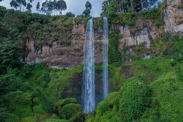 Aerial view of a majestic waterfall cascading down a verdant cliff face, framed by lush greenery and towering trees, Sipi Falls, Eastern Region, Uganda.