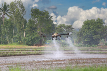 A drone effectively sprays pesticide over a farm field surrounded by lush green trees.