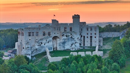 Aerial photograph showing the medieval castle ruins in Ogrodzieniec, Poland during sunrise, surrounded by dense forest and warm morning light