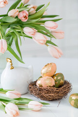 Beautiful Easter greeting card. A bouquet of delicate tulips, a chicken, and eggs with a golden pattern on a table in a white kitchen interior.