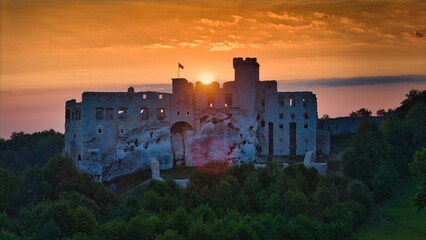 Aerial photograph showing the medieval castle ruins in Ogrodzieniec, Poland during sunrise, surrounded by dense forest and warm morning light