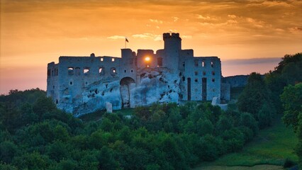 Aerial photograph showing the medieval castle ruins in Ogrodzieniec, Poland during sunrise, surrounded by dense forest and warm morning light
