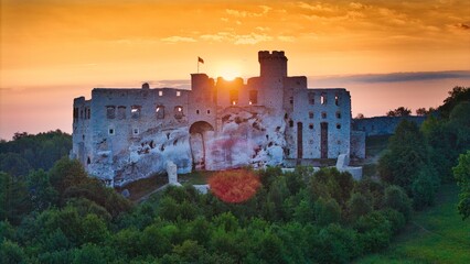 Aerial photograph showing the medieval castle ruins in Ogrodzieniec, Poland during sunrise, surrounded by dense forest and warm morning light