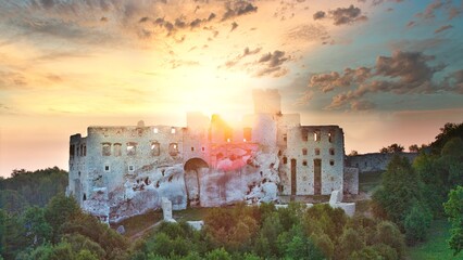 Aerial photograph showing the medieval castle ruins in Ogrodzieniec, Poland during sunrise, surrounded by dense forest and warm morning light
