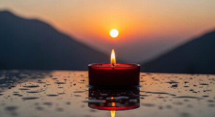 A solitary red candle burns brightly reflecting on a wet surface against a dramatic mountain sunset backdrop