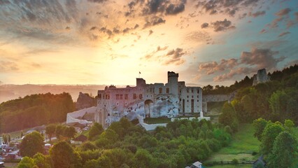 Aerial photograph showing the medieval castle ruins in Ogrodzieniec, Poland during sunrise, surrounded by dense forest and warm morning light
