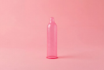 Pink condom arranged against a solid pink background symbolizing safe sex and contraception awareness.