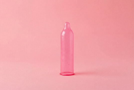 Pink condom arranged against a solid pink background symbolizing safe sex and contraception awareness.