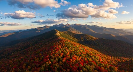 Autumn foliage blankets mountain range beneath a picturesque cloudscape at sunrise
