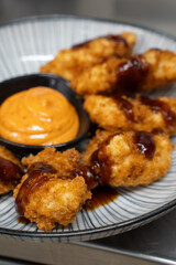 Crispy chicken nugget over plate with nuggets and sauce.