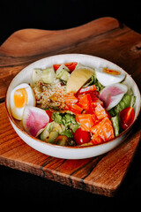 Fresh salad bowl with salmon, vegetables, and egg served on wooden table