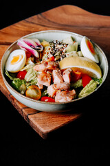 Healthy chicken salad with fresh vegetables and eggs served in a bowl on a wooden board