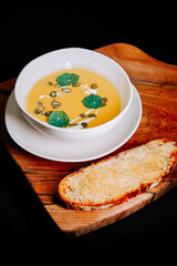 Creamy soup served in a bowl with fresh leaves and toasted bread on a wooden plate