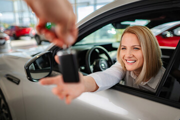 Happy woman buying new car receiving keys at dealership