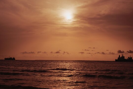 Bonny Island, Nigeria - 06 April 2025: View of ships silhouetted against the fiery horizon, where the sun bleeds into the tranquil waters, creating a scene of serene maritime activity.