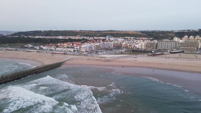 Aerial view of the sandy Costa da Caparica beach meeting the city buildings under a cloudy sky, Costa da Caparica, Setubal, Portugal.