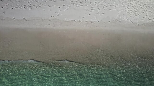 White sand dunes meet the emerald Gulf of Mexico under a bright blue sky. A wide shot captures beachgoers enjoying the clear water and sunny, pristine shoreline.