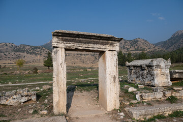 An ancient stone gate and sarcophagus standing in front of mountains and a rural backdrop in the necropolis area of Hierapolis. Historical heritage.