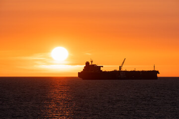 Obraz premium Silhouette of a large cargo ship sailing on the Baltic Sea near Estonia during a dramatic golden orange sunset
