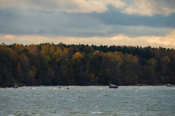 Scenic view of the choppy Baltic Sea coast with rocky shore and colorful autumn forest in Estonia under cloudy sky
