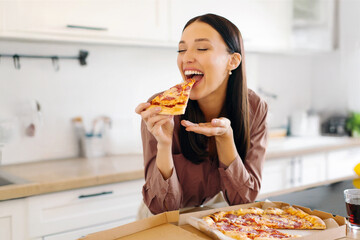 The joy of pizza. Excited woman enjoying tasty pizza, holding and biting slice with closed eyes,...