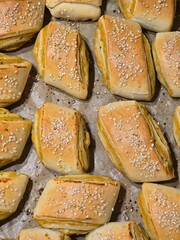 Close-up of freshly baked, golden Paszteciki (Polish savory pastries) filled with a yellow stuffing and generously topped with white sesame seeds on parchment paper.