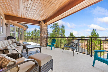 A balcony with a couch, chairs, and a table overlooking a forest