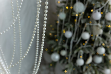 The artificial Christmas tree, made of environmentally friendly materials, is decorated with white plastic balls and pearl beads. Christmas tree in the interior of a residential building