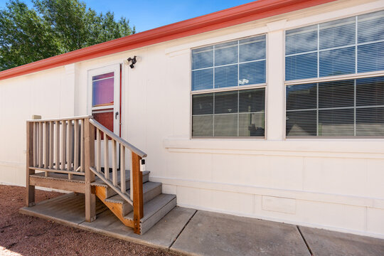 A beautiful white mobile home featuring stairs and a vibrant red door