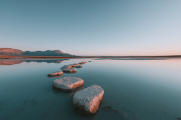 Stepping stones create peaceful pathway across calm reflective water toward distant mountains.