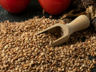 A bag of buckwheat groats and loose groats scattered with a wooden spoon on a dark stone table