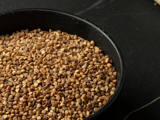 Detail of a bowl of raw buckwheat on a dark stone table