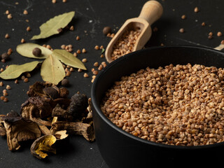 A bowl of raw buckwheat groats and dried mushrooms next to it on a dark stone table