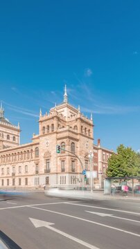 Panorama showing Cavalry Academy timelapse in Plaza de Zorrilla, Valladolid, Spain. Historic military building with intricate architecture, surrounded by busy urban scene under a blue sky with clouds