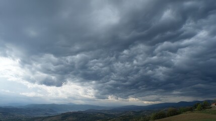 Fototapeta premium A dramatic sky filled with dark clouds looms over peaceful hills in evening light.