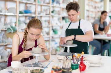 Students teenage girl and teenage boy sculpt ceramic product from raw clay in workshop