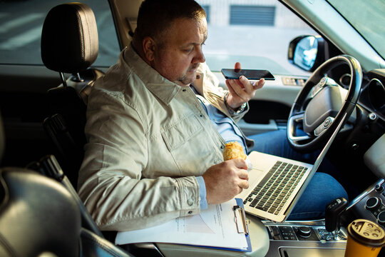Adult man focused, working on laptop and phone in parked car - Powered by Adobe