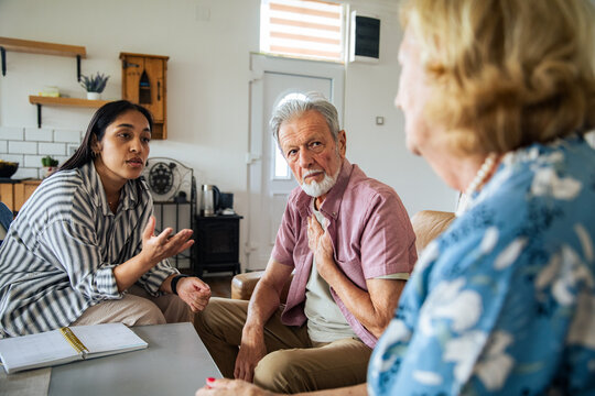 Young adult counselor discussing options with concerned senior couple at home