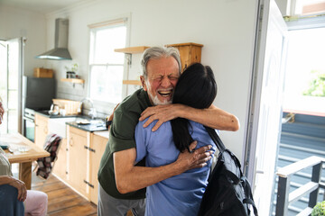 Senior man joyfully hugging adult caregiver at home doorway