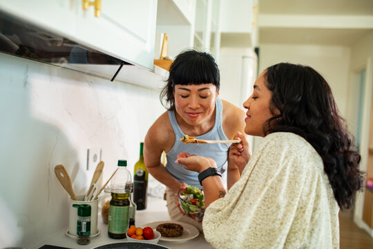 Adult lesbian couple tasting dinner in home kitchen, happy
