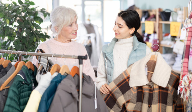 Elderly and young women buyers choosing warm coat or down jacket in clothing store