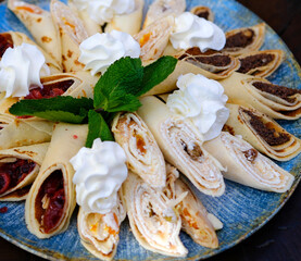 A beautifully layered crepe cake sits on a white pedestal, adorned with whipped cream, strawberries, and blueberries. High quality photo