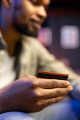 African american man entering banking credentials for online shopping, sitting on the couch to purchase during sale season. Young adult transferring money to pay for his web orders.