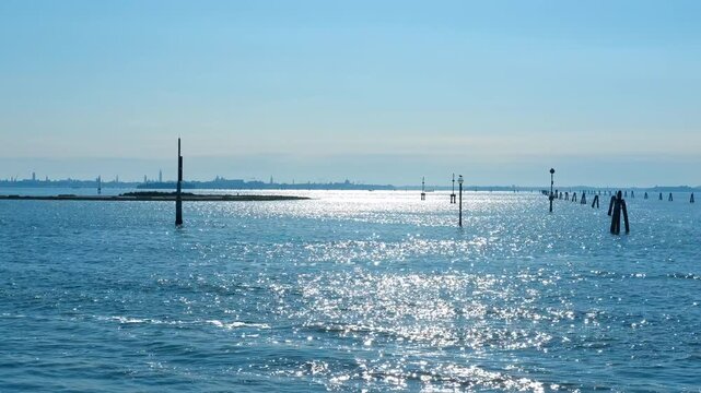 Sun glittering on calm venetian lagoon waters. Glistening venetian lagoon waters shimmering under bright midday sunlight, showcasing navigation poles guiding boats through serene blue channel
