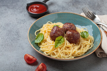 Plate of spaghetti topped with meatballs and basil leaves, accompanied by tomato sauce, fork, spoon, napkin, and tomato slices, healthy home cooking