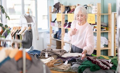 Mature woman spend time in shop and chooses sweater. Changing wardrobe, shaping style of clothing, filling wardrobe with modern stylish clothes. Chain store of affordable clothing