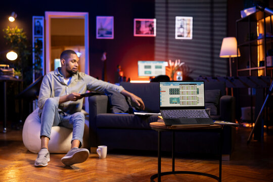 African American freelancer studies candlestick charts on a laptop in his living room. Day trader monitoring stock exchange data, growth trends and financial figures while working remotely.